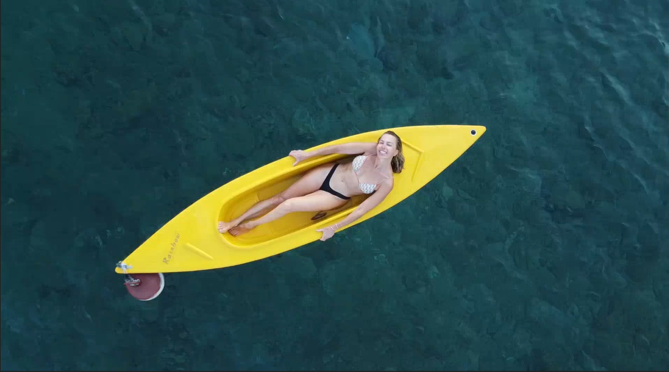 Esther Sarphatie lying back in a yellow kayak on calm blue water, smiling.