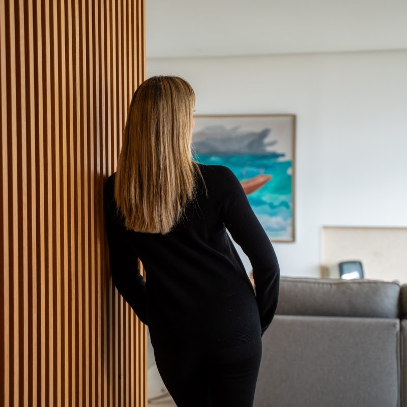 Back view of Esther Sarphatie standing beside a wooden slat wall.