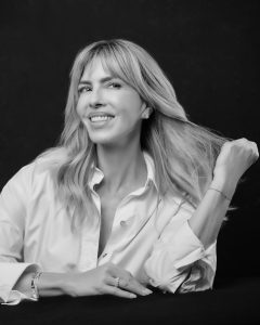 Black-and-white portrait of Esther Sarphatie smiling in a white shirt, holding her hair to the side.