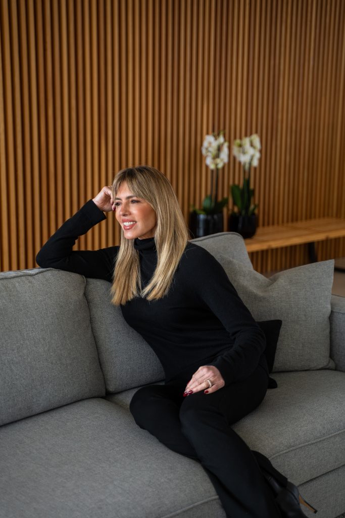 Esther Sarphatie smiling while seated on a couch with white orchids behind her.